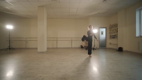 a group of young ballet students in black dancewear practicing positions in a spacious ballet studio with wooden flooring and wall-mounted barres. focused expressions and synchronized movements.