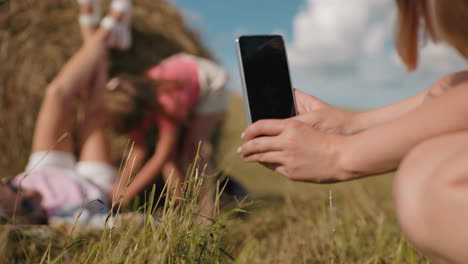 fotógrafo capturando la imagen de un amigo acostado en una bala de heno mientras otra persona camina en un entorno rural soleado, destacando el ocio al aire libre, la amistad y la creatividad en la naturaleza