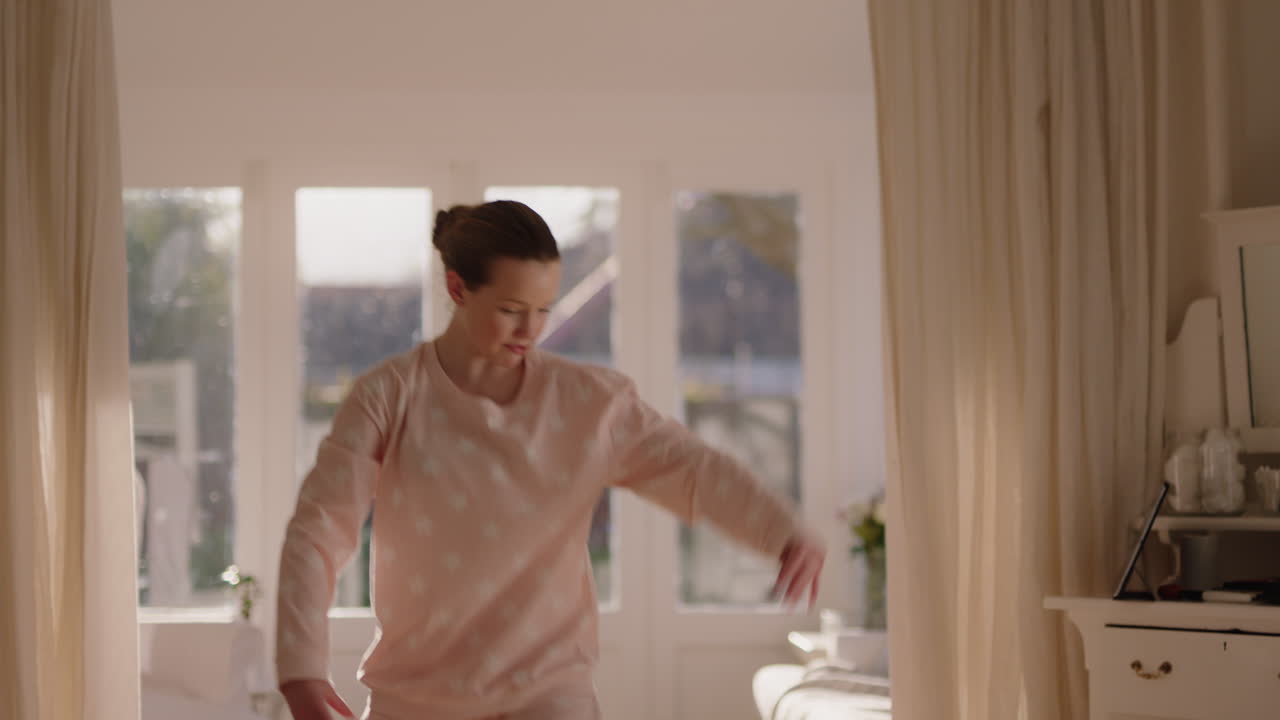 아름다운 십대 발레리나 소녀가 침실에서 발레 춤을 연습하고 주말 아침에 파자마를 입고 해가 뜨면 춤을 연습합니다.