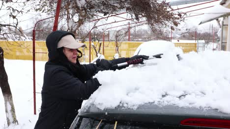 woman removing snow from vehicle with snow brush - close up