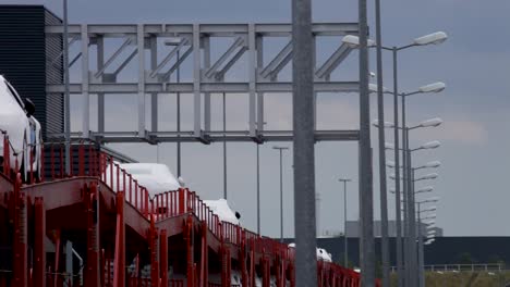 red train cars loaded with new automobiles under an industrial metal structure, daytime