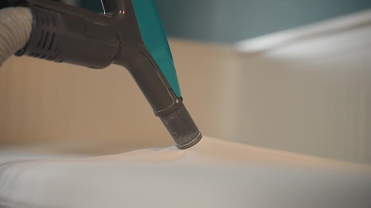 Professional mattress cleaning demonstration with nozzle, operator hand guiding handheld extractor across fabric, strong suction and hose movement lifting dust, modern bedroom background, efficient