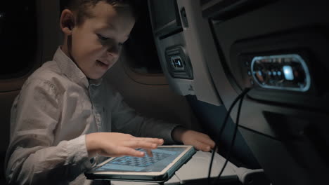 niño con almohadilla en el avión que entretiene con un juego de ajedrez