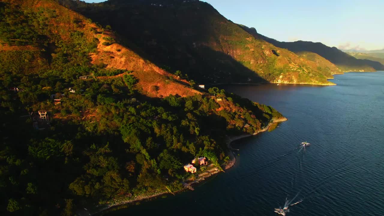 Zoom indietro aereo che rivela la luce dell'ora d'oro sul litorale del lago Atitlán, le colline e l'acqua calma e distesa