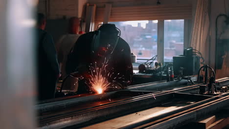 A welder in protective gear works on metal, producing bright sparks in a workshop setting