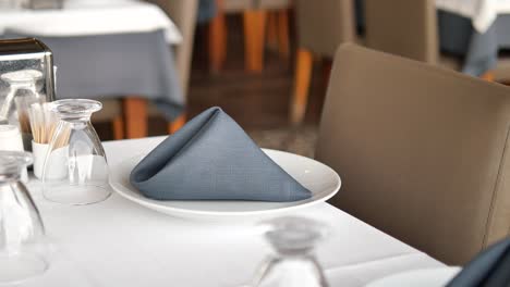 a restaurant table is set with a white tablecloth, white plates, and gray napkins.