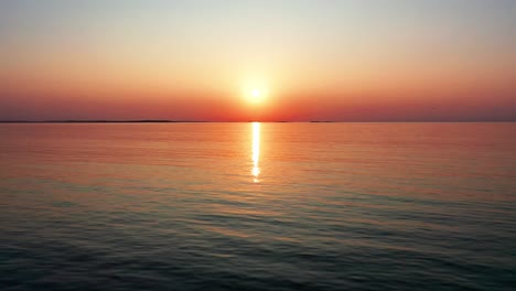 gorgeous ocean sunset with bright glowing sun casting colorful red, orange, purple and yellow reflections over peaceful rippling waves of the sea