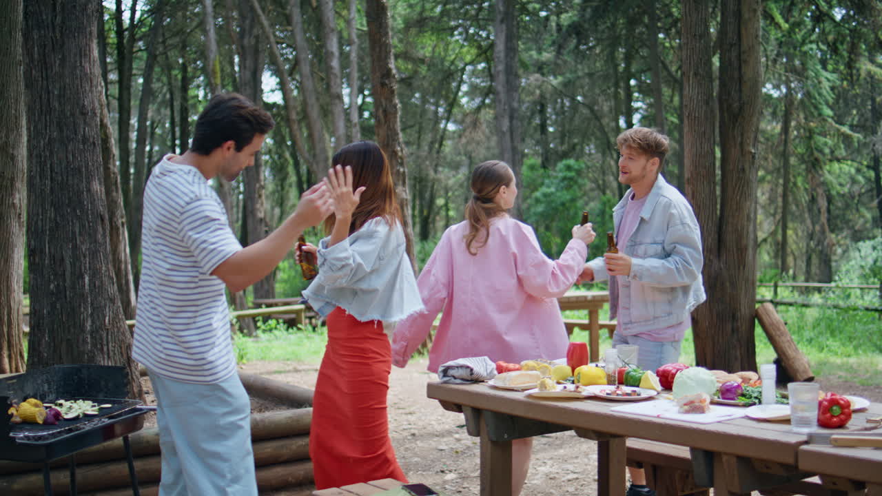 Joyful friends dancing picnic party in green forest. Happy buddies