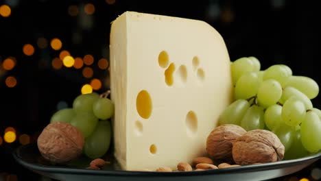 close up part of medium hard cheese head edam gouda parmesan on wooden board, with nuts and grapes rotaiting on the plate