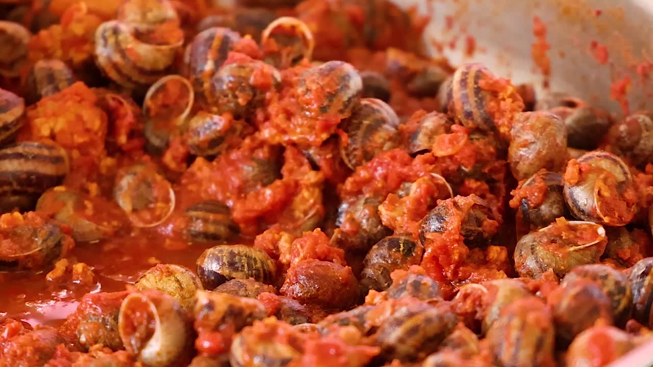 Un primo piano dettagliato di numerose lumache che cuociono in una salsa al pomodoro saporita e ribollente.