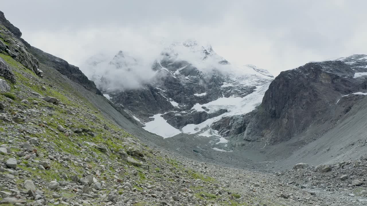 vista de drones sobre un desolado glaciar alpino en retroceso rodeado de montañas y rocas y picos cubiertos de nieve