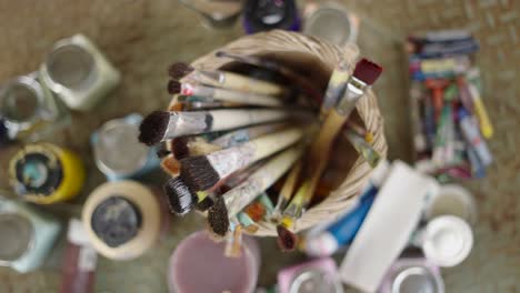 collection of paintbrushes in a woven basket surrounded by art supplies