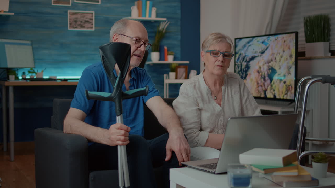 Elderly Couple Using Laptop at Home with Crutches and Walker