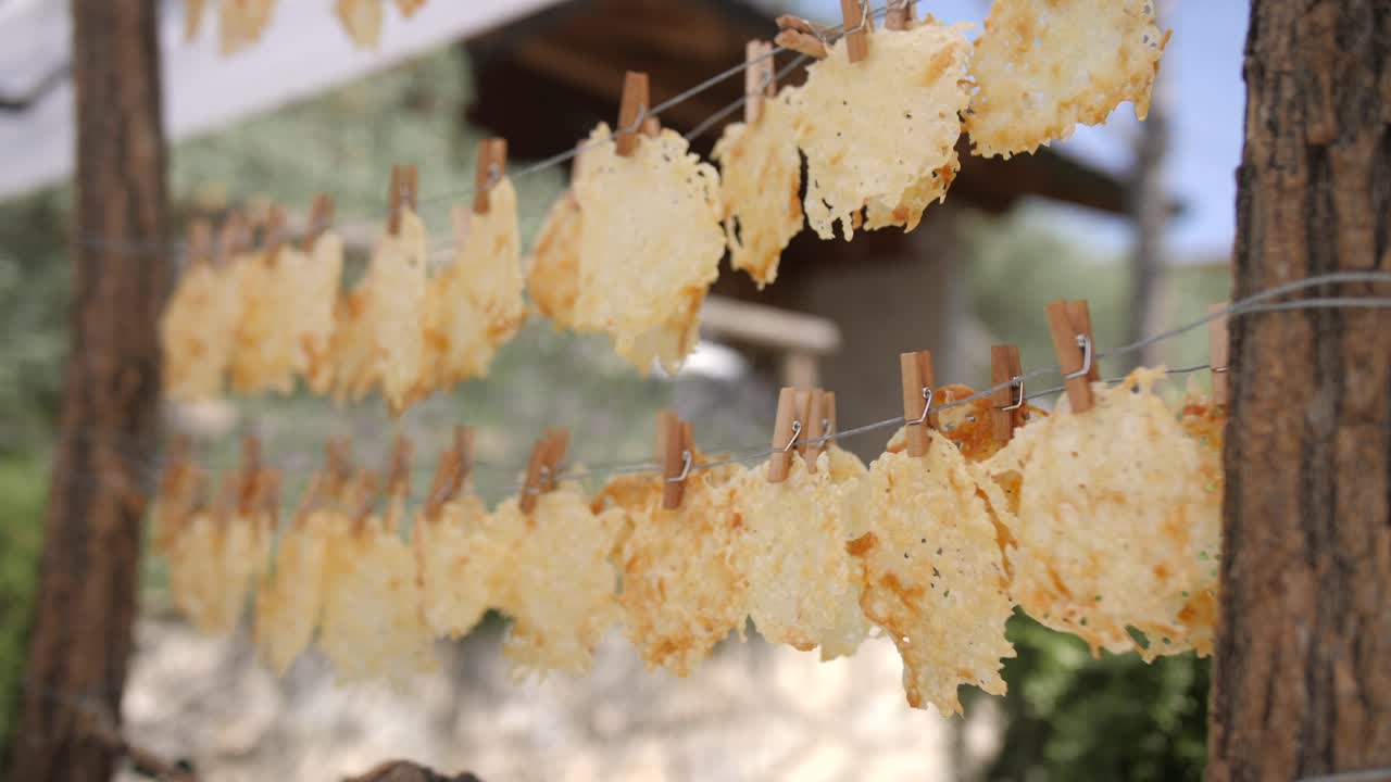 Crispy cheese chips hanging on a clothesline with wooden clips, outdoor rustic setting