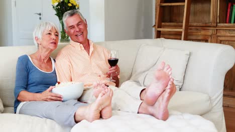 Älteres-Paar-Trinkt-Popcorn-Und-Ein-Glas-Wein-Im-Wohnzimmer