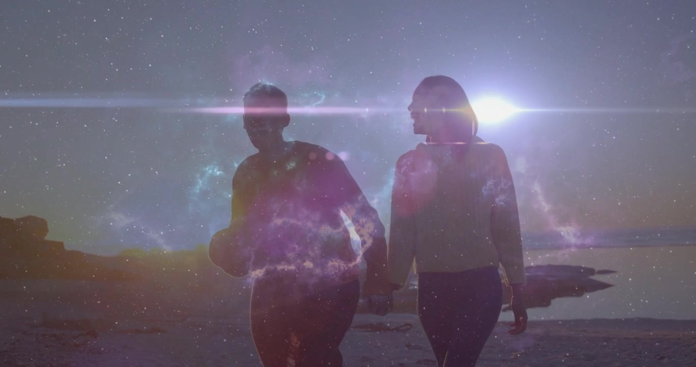 Film couple walking on beach sharing glance approaching center shimmering nebula flare backlighting