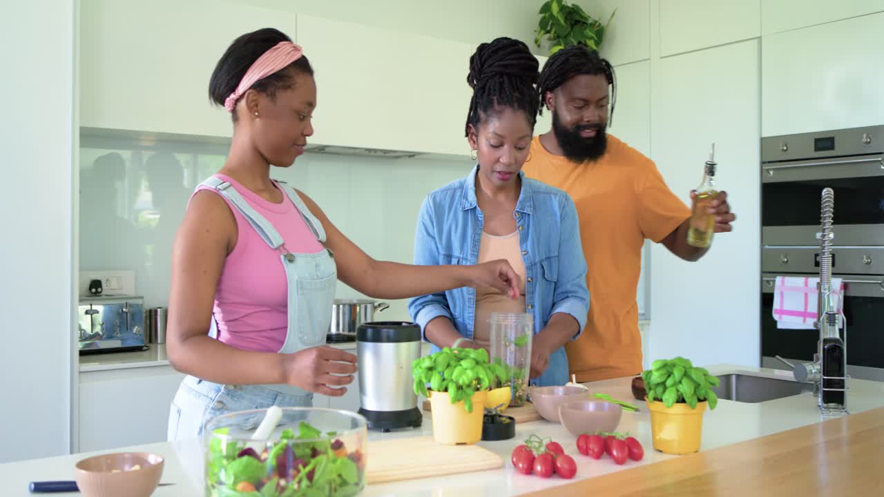 Afroamerikansk familie starter måltidsforberedelsen, forbereder ingredienser ved køkkenøen med en blender.