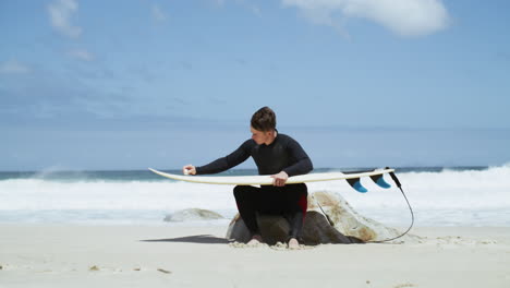 a young man rubbing wax on a surfboard