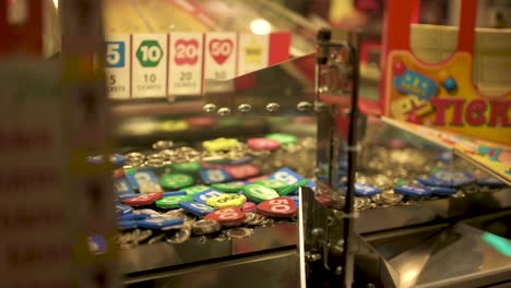 Arcade-coin-pusher,-dropping-and-pushing-coins-with-tickets-coming-out,-slow-motion