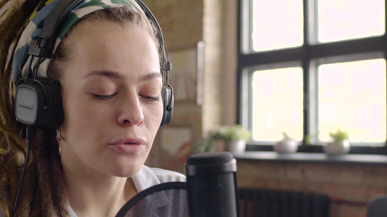 헤드폰을 끼고 팟캐스트를 녹음하는 동안 마이크에 대고 말하는 여성의 모습을 클로즈업