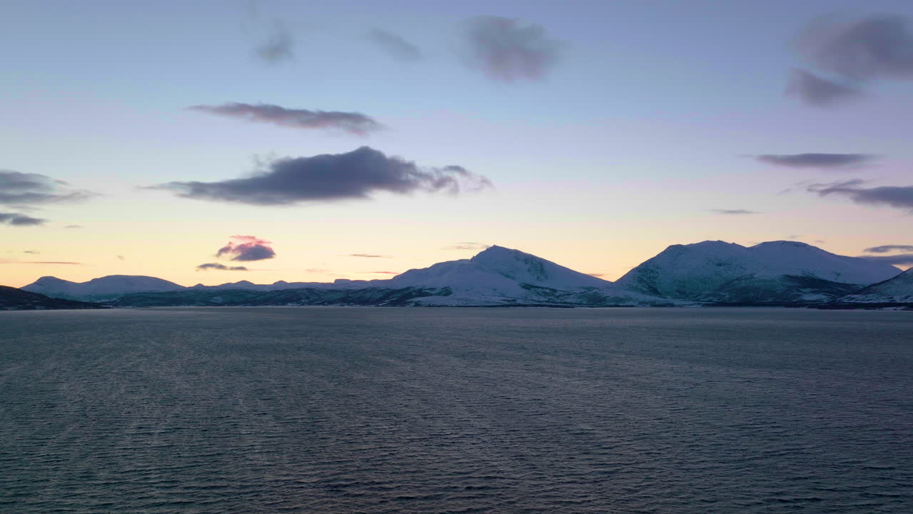 석양에 눈 덮인 산을 향해 물 위로 낮게 날아가는 드론 샷