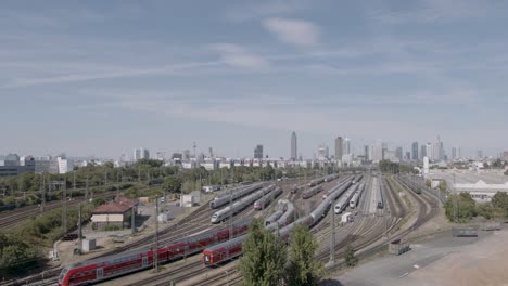 a wide aerial shot of frankfurt's railway yard with a mix of trains and city skyline in the background under blue skies