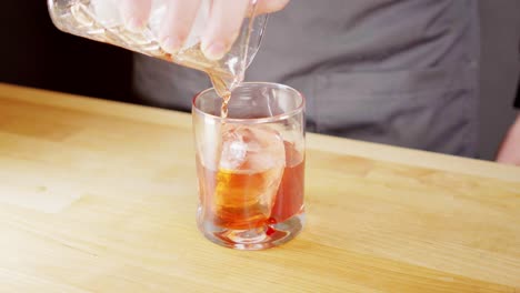 pouring a negroni from a mixing glass