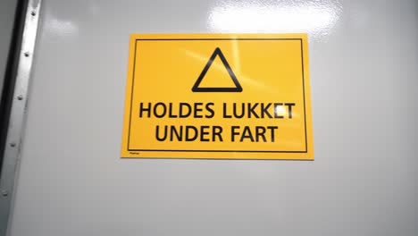 sign on watertight door in ships engine room warning that door should always be closed at sea - approaching big yellow sign with norwegian language