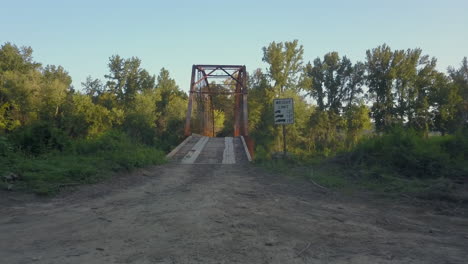 dolly in to pedestal up shot of an old iron bridge over a tree lined rural river in warm late afternoon light