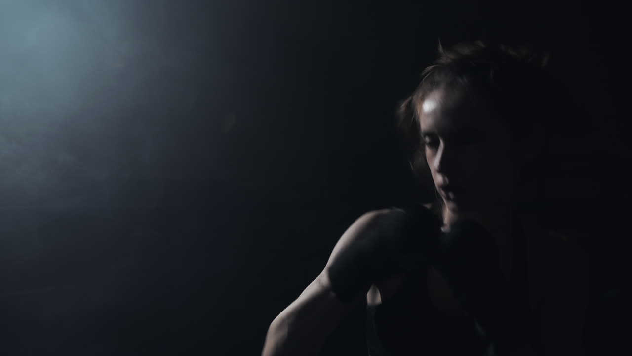 Female Boxer Training in a Dark, Smoky Gym with Spotlight