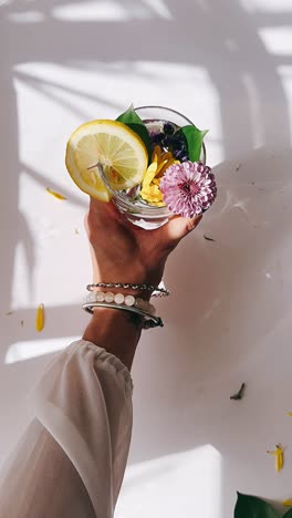 hand holding a glass of floral infused water with lemon