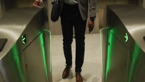 sección media de un hombre de negocios afroamericano que llega a una oficina moderna usando un pase en las puertas de seguridad