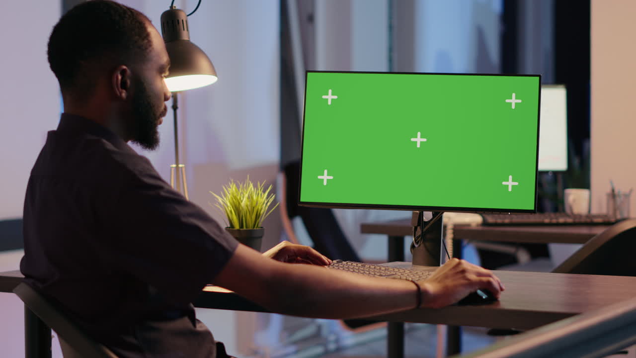 Man working on computer with green screen in office