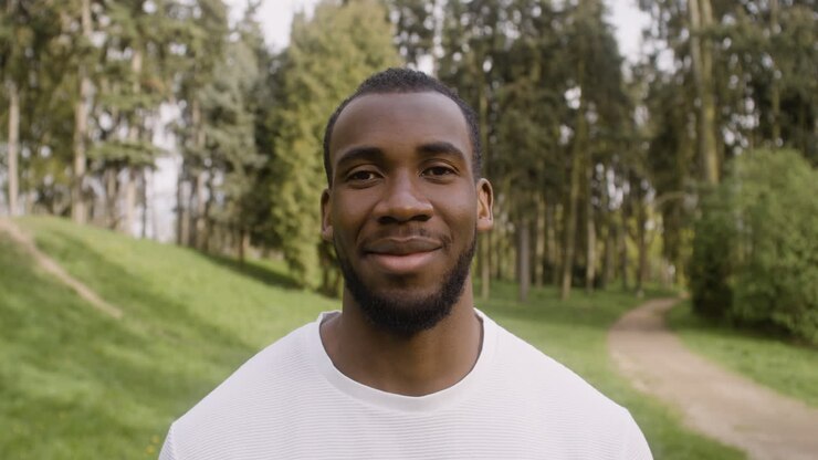 Portrait d'un homme américain debout dans le parc, regardant l'appareil photo et souriant