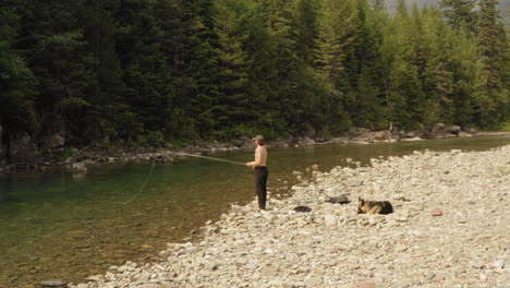 Pesca-Con-Mosca-En-Mcdonald-Creek-En-El-Parque-Nacional-De-Los-Glaciares---Un-Hombre-Echando-Moscas-Mientras-Su-Perro-Leal-Espera-Pacientemente-En-El-Banco