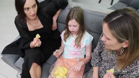women and girl eating chips on the couch