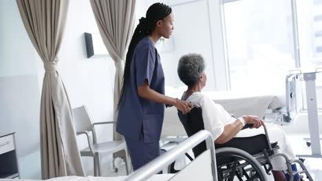 african american female doctor talking with senior woman in wheelchair in hospital room, slow motion