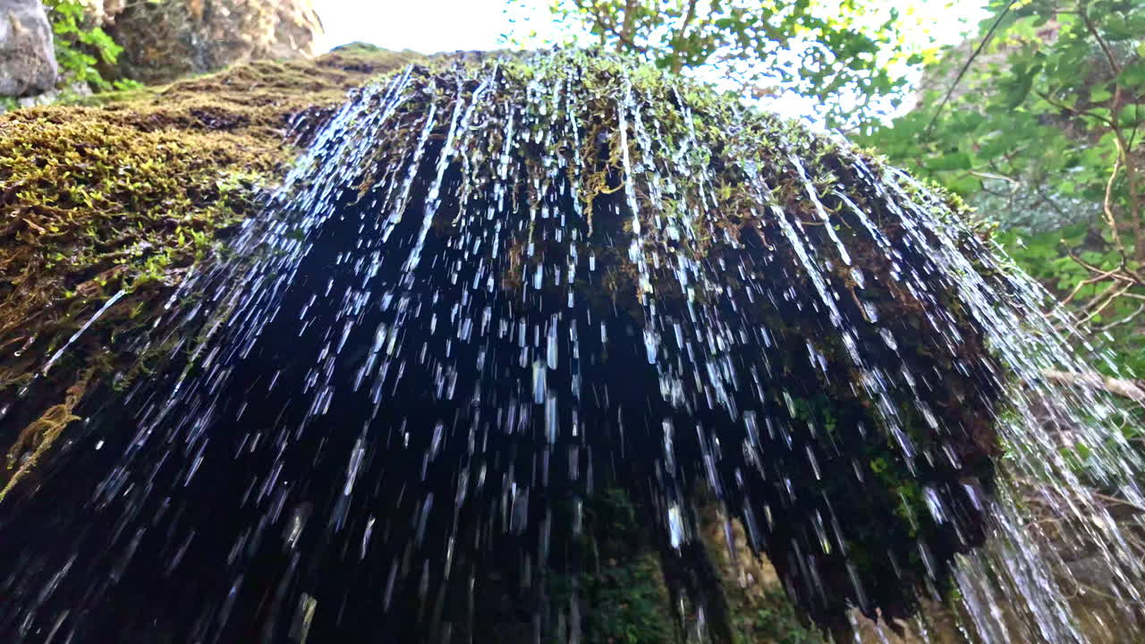 Water gently cascades over mossy rocks at Richtis Waterfall in Greece on a sunny day