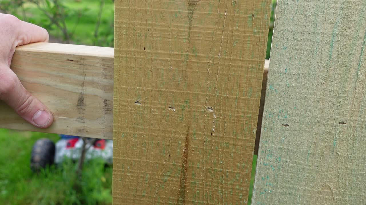 Hands of person use pneumatic nail gun for wooden fence, close up