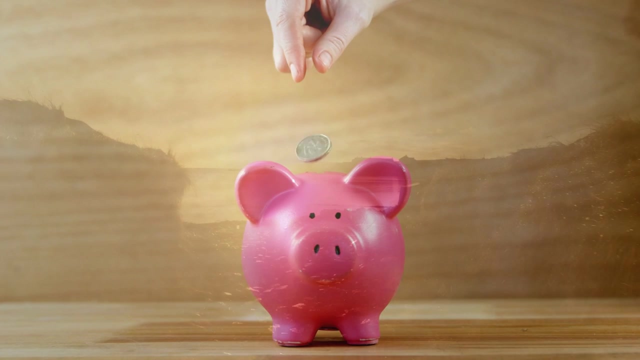 Human hand entering, lowering and releasing coin over pink piggy, coin ricocheting left for saving
