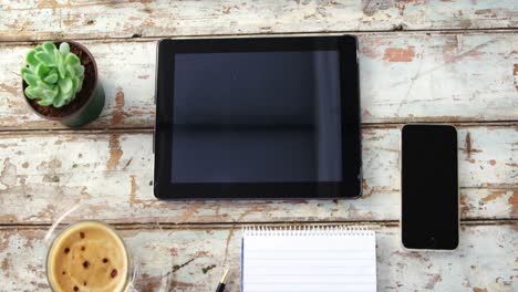 Coffee-cup,-digital-tablet,-mobile-phone,-notepad-on-wooden-plank