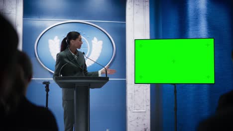 organization female representative speaking at press conference in government building with green screen mock up on display. press officer delivering a speech at summit. minister in congress.