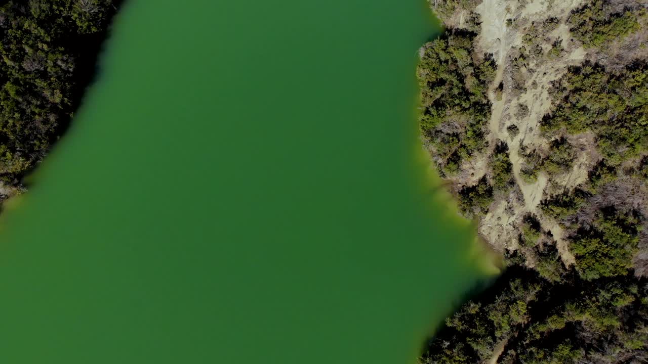 Green lake with deep clear water surrounded by mountains slopes on valley with lush vegetation and dry bushes