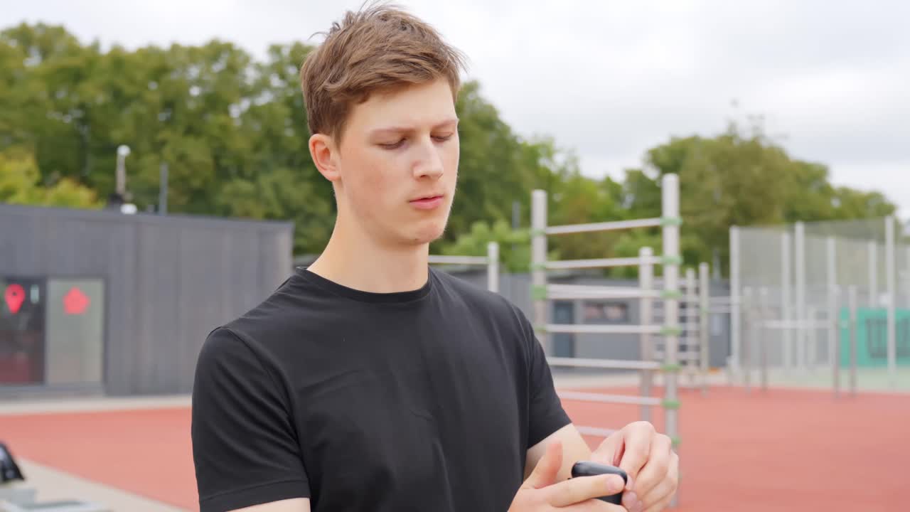 Young man puts in earbuds while preparing to train outdoors at park, side profile view