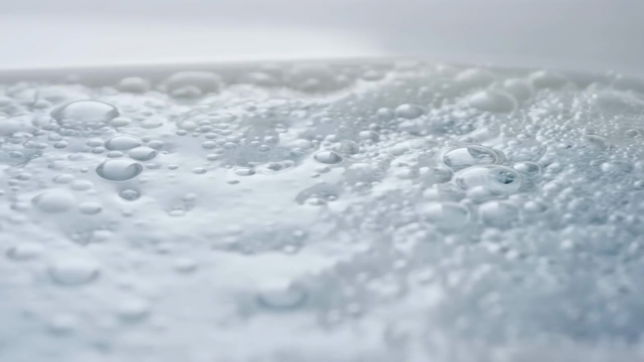 Vista de cerca de espuma blanca pálida cubierta con pequeñas burbujas y suaves ondas, creando una textura suave y brillante, tonos neutros brillantes y un fondo abstracto higiénico y tranquilo con enfoque superficial y suave