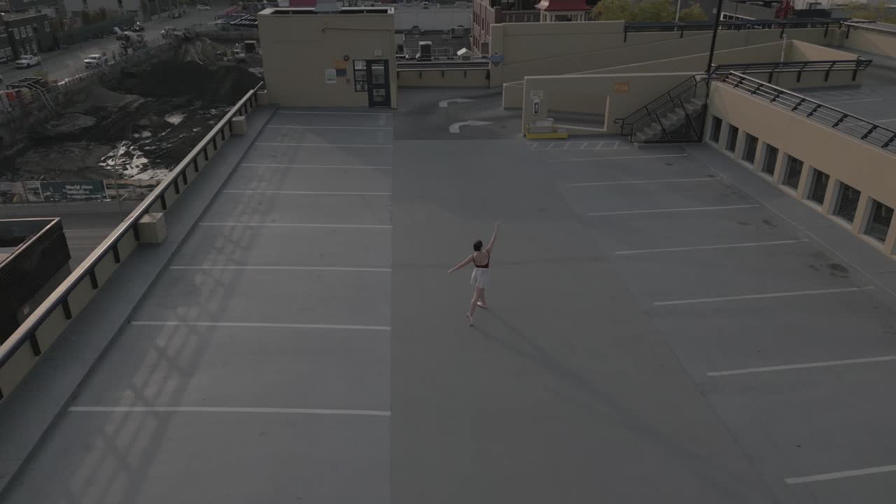 Afastamento amplo de drone de uma bailarina na cobertura de um estacionamento.