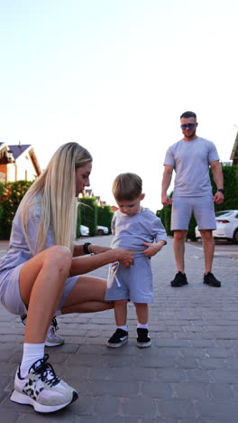 family fun during summer evening walk. a woman kneels to adjust a child's outfit as a man stands by, enjoying a relaxed evening in their neighborhood