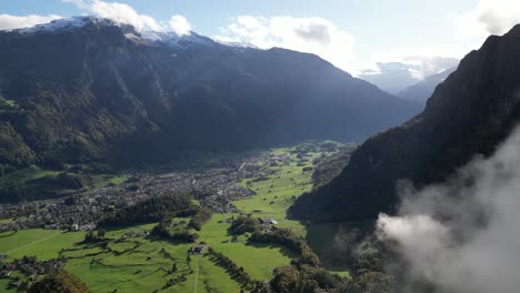 Aerial-view-of-forward-panning-shot-of-green-valley-area-slowly-uncovered-through-the-clouds-surrounded-by-the-high-mountain-peaks