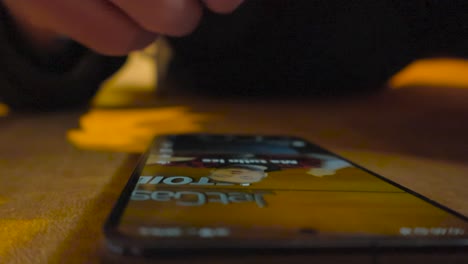 caucasian european person scrolling social media vertical videos on his smartphone close up in slow motion on an orange couch while person is lying down. person wears plack clothing and his hand close