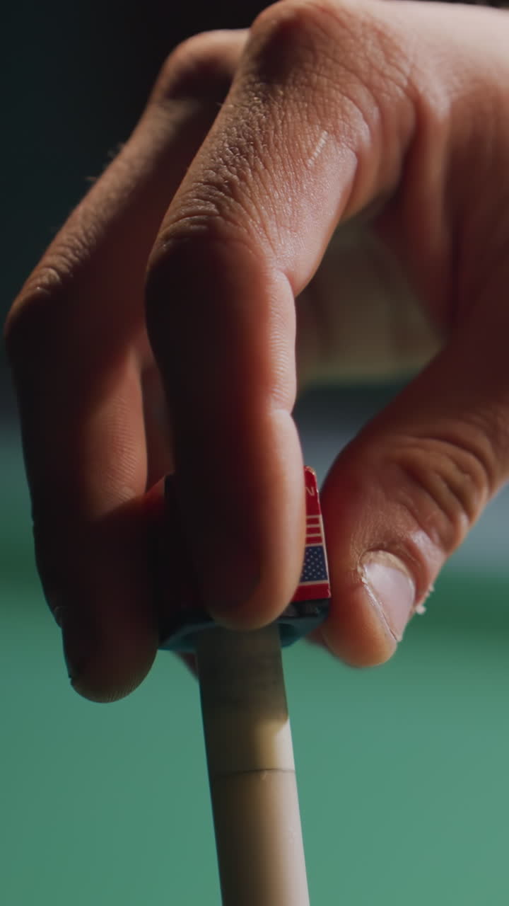 Close-up of male hand carefully applying chalk to cue stick before executing precise shot on green pool table. Focus on preparation, skill, and accuracy in billiards with blurred balls in background